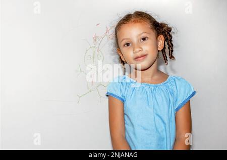 Piccola ragazza brasiliana che scarabocchio, dipinge e disegna su una parete di colore giallo chiaro Foto Stock