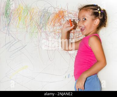 Piccola ragazza brasiliana che scarabocchio, dipinge e disegna su una parete di colore giallo chiaro Foto Stock