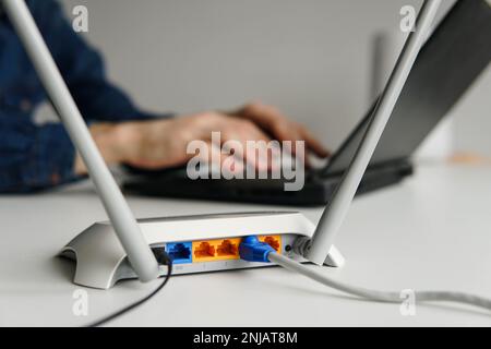 Router wifi wireless ad alta velocità sul tavolo. Uomo che usa il notebook in background Foto Stock