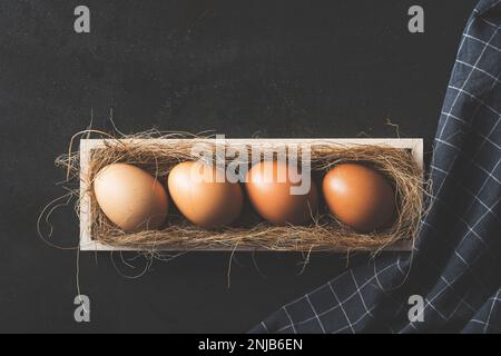 Uova allineate in fila in cassa di legno su fondo nero rustico Foto Stock