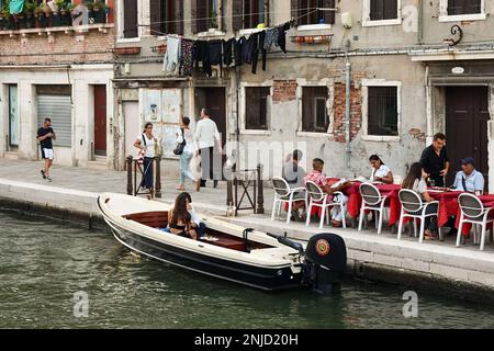 Ristorante sul lungomare di Fondamenta dei Ormesini con vista sul Rio della Misericordia con giovane coppia che ha aperitivo su una barca ormeggiata, Venezia, Italia Foto Stock