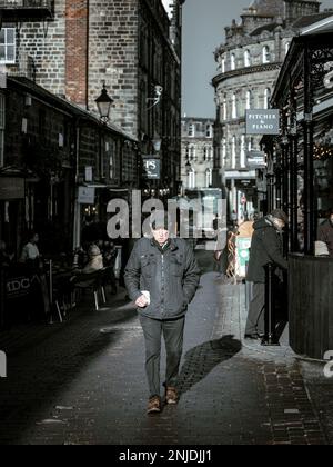 Un uomo cammina da solo per le strade acciottolate di Harrogate, inondato dalla luce soffusa dell'inverno mentre gli edifici storici e la vita quotidiana si svolgono intorno a lui Foto Stock
