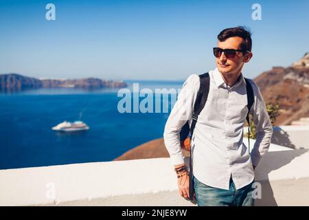 Santorini viaggiatore uomo godendo Fira o Thera paesaggi città, Grecia. Turistico con zaino a piedi sull'isola ammirando il mare. Turismo, viaggi, sumo Foto Stock