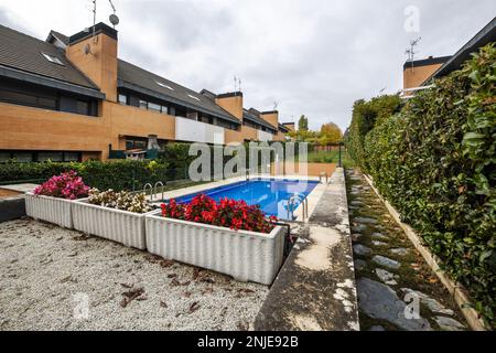 Piscina estiva privata di uno sviluppo di case semi-indipendenti singole-familiari residenziali circondate da siepi, erba e vasi di fiori Foto Stock