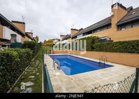 Piscina estiva privata di uno sviluppo di case unifamiliari semi-indipendenti circondate da siepi, erba e pentole, un passaggio in pietra e erba e un metallo Foto Stock