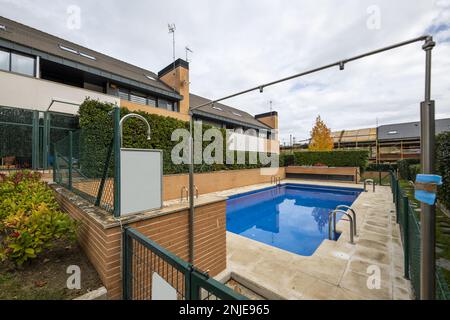 Piscina estiva privata di uno sviluppo di case unifamiliari semi-indipendenti circondate da siepi, erba e pentole, pietra e erba passerella, arco con sho Foto Stock