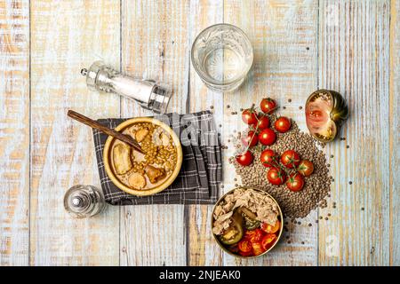Vita morta con tradizionale stufato di lenticchie in una ciotola di legno e insalata di tonno e pomodoro in una ciotola dorata su un tavolo di legno chiaro Foto Stock