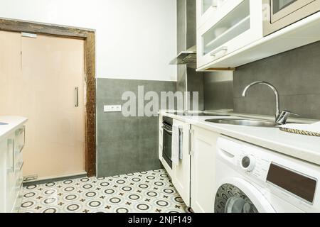 Cucina con mobili bianchi in un appartamento per vacanze con pavimenti in gres idraulico Foto Stock