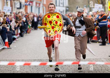 La gara annuale di frittelle del martedì Shrove si tiene a Lichfield, Staffordshire, Inghilterra. La manifestazione comprende gare per bambini, una gara di mascotte e razze maschili e femminili. L'evento inizia a mezzogiorno e viene condito dal grido della città e giudicato dal sindaco. Nella foto a sinistra, indossando la frittella, vincitore dell'evento di divertimento per mascotte Austin Brauser del WIP Running Club. Foto Stock