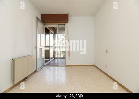 Camera da letto vuota con pareti bianche, radiatore in alluminio, uscita sulla terrazza con pavimenti in terrazzo e finestre in alluminio e vetro Foto Stock