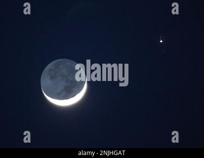 La sera del 22 febbraio 2023 convergono una luna dibbosa cerante e il pianeta Giove. Tre lune galileiane di Giove sono visibili. Foto Stock