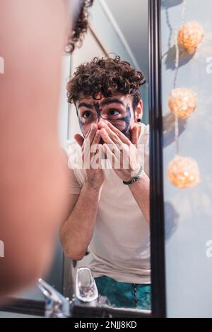 L'uomo omosessuale che si lava il viso dopo aver applicato la maschera facciale in argilla per la cura della pelle. Routine di bellezza. Foto Stock
