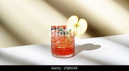 Bevanda alcolica di mele con vodka, liquore di mele, cannella, limone, guarnita con rosmarino. Sfondo beige chiaro, luce forte, ombra pat Foto Stock