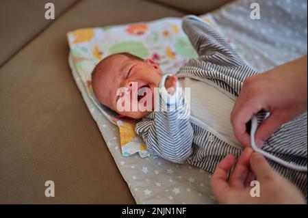 Madre che indossa abiti sulla bambina che piange Foto Stock