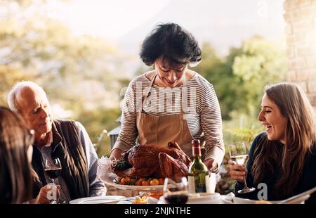 Tutti amano mamme tacchino farcito. Una donna matura che porta un tacchino appena cucinato al tavolo da pranzo il giorno del Ringraziamento. Foto Stock