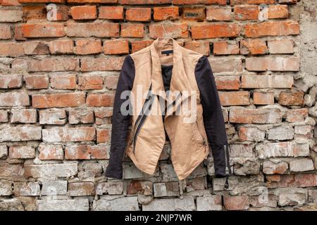 giacca donna marrone appesa su grucce su un vecchio muro di mattoni a casa sulla strada, moda donna Foto Stock