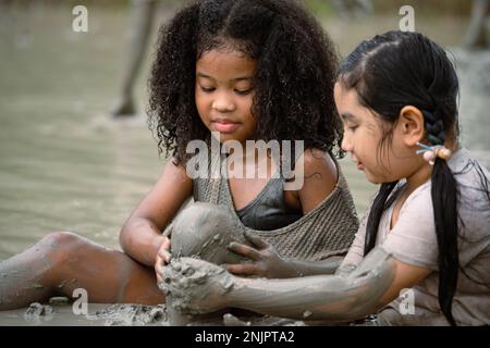 Gruppo di ragazze felici che giocano in pozza di fango bagnato il giorno d'estate nella stagione piovosa Foto Stock