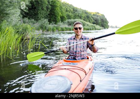 Kayak sul fiume. Un giovane caucasico siede in un kayak e pagaie. Il concetto di intrattenimento acquatico. Foto Stock