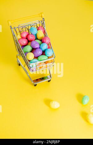 Happy easter.Shopping cart con glitter colorati uova di pasqua sul giallo background.Top view. Foto di alta qualità Foto Stock