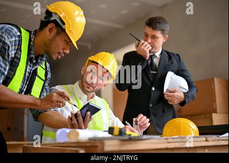 Team di ingegneri edili e uomini d'affari che lavorano insieme nel cantiere, controllando la scala su BluePrint, utilizzando walkie talkie. Foto Stock