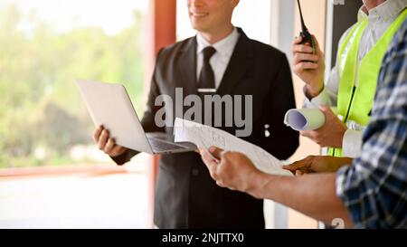 Immagine ritagliata di un uomo d'affari caucasico di successo in un abito formale d'affari ispeziona l'edificio presso il sito con un team di costruzione. Ingegnere e. Foto Stock