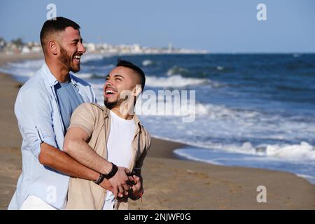 Bella coppia gay sorridente mentre si rilassa sulla spiaggia insieme. Foto Stock