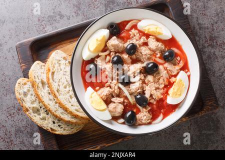 Tradizionale insalata murciana Mojete fatta di pomodoro, tonno in scatola, olive nere, uovo sodo e cipolla closeup sul piatto sul legno. Orizzontale t Foto Stock