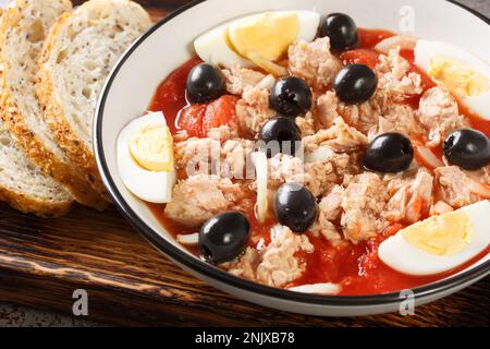 Tradizionale insalata murciana Mojete fatta di pomodoro, tonno in scatola, olive nere, uovo sodo e cipolla closeup sul piatto sul legno. Orizzontale Foto Stock