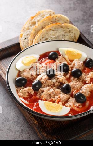 Insalata Murcian la ensalada murciana con pomodoro, tonno in scatola, olive nere, uovo e cipolla primo piano sul piatto della tavola di legno. Verticale Foto Stock