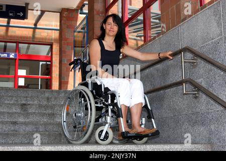 donna su una sedia a rotelle su una scala della stazione ferroviaria, non priva di barriere Foto Stock