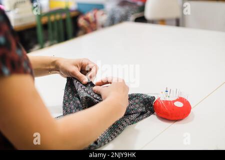 Anonimo donna designer in maglia casual cucito modello su tessuto con ago in atelier creativo Foto Stock