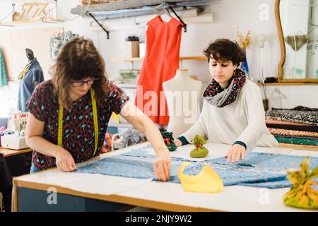 Sartorie femminili concentrate in abiti casual che preparano il modello mentre lavorano con tessuti colorati in atelier Foto Stock