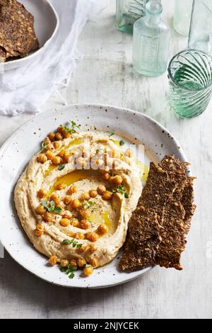 Vista dall'alto del delizioso hummus con semi di ceci e olio d'oliva servito su piatto con croccanti e sani cracker sul tavolo in cucina Foto Stock