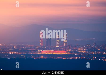 Vista aerea del paesaggio urbano con grattacieli illuminati ed edifici sotto il colorato cielo del tramonto a Madrid Foto Stock
