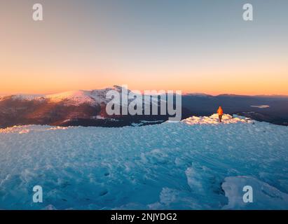 Vista pittoresca del viaggiatore senza volto che si erge su una collina innevata sul Monte Bola del Mundo durante il tramonto in Spagna Foto Stock