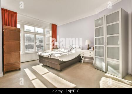 Interno di spaziosa camera da letto luminosa con comodo letto matrimoniale coperto con coperta posta contro guardaroba in legno e comò nelle giornate di sole Foto Stock