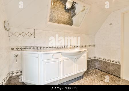 Design interno di bagno chiaro con armadio bianco sotto il lavabo posto su pavimento piastrellato in marmo e specchio rettangolare Foto Stock
