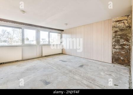 Design interno di camera spaziosa e luminosa con grandi finestre e radiatori con nuove carte da parati beige sulle vecchie pareti e pavimento in cemento Foto Stock