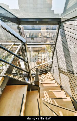 Dall'alto di scale a rulli in legno con ringhiere collocate in un edificio contemporaneo con pareti di vetro alla luce del sole Foto Stock