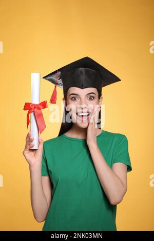 Studente emozionale con cappello di laurea e diploma su sfondo giallo Foto Stock