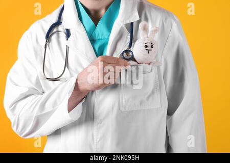 Pediatra con coniglio giocattolo e stetoscopio su sfondo giallo, primo piano Foto Stock