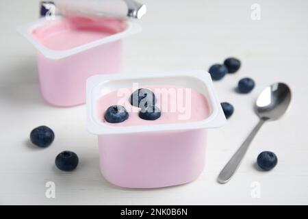 Tazza di plastica con gustoso yogurt e mirtilli su un tavolo di legno bianco Foto Stock