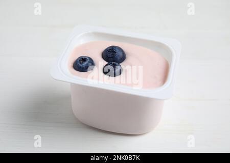 Tazza di plastica con gustoso yogurt e mirtilli su un tavolo di legno bianco Foto Stock