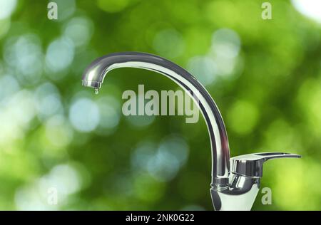 Goccia d'acqua che scorre dal rubinetto all'aperto nelle giornate di sole, effetto bokeh Foto Stock