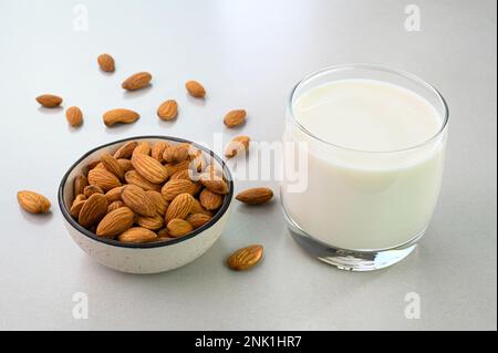 Latte di mandorla in una tazza di vetro con mandorle in una ciotola Foto Stock