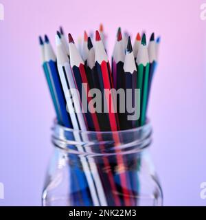 Contenitore matita per la creatività, l'arte e il disegno per la colorazione scuola cancelleria zoom. Primo piano di un vaso di vetro con matite colorate in studio sfumato viola Foto Stock