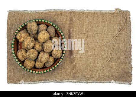 Noci nel guscio in una ciotola di argilla sullo sfondo di burlap. Isolato su sfondo bianco. Vista dall'alto. Foto Stock