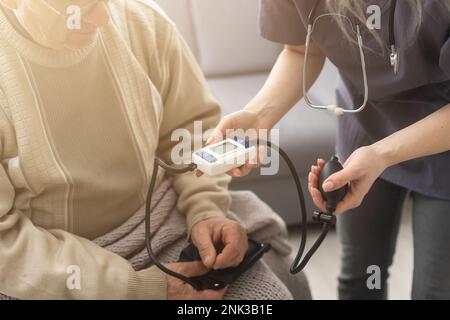 Giovane infermiera sorridente che prende la pressione sanguigna del vecchio Foto Stock