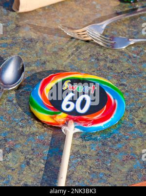 Un grande lollipop colorato si posa sul tavolo del partito con un adesivo Sweet 60 per la ragazza di compleanno che ha girato sessant'anni Foto Stock