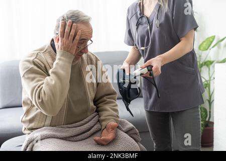 Giovane infermiera sorridente che prende la pressione sanguigna del vecchio Foto Stock